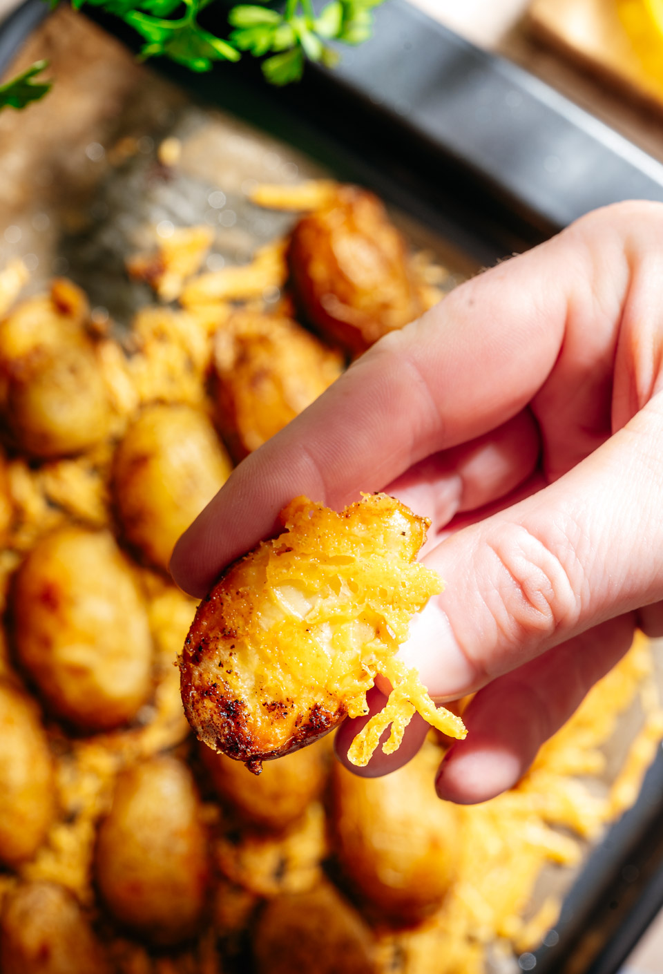 Close-up foto van een hand die een aardappel uit de oven vast heeft met een krokant laagje kaas