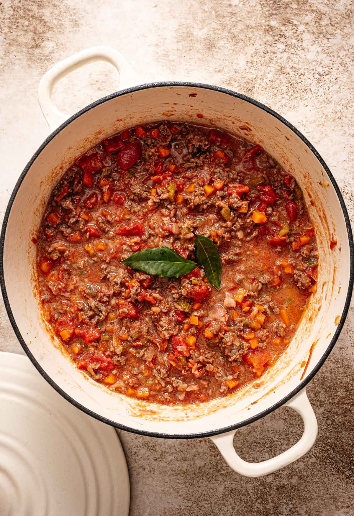 Stap 4- gepelde tomaten, bouillon en tomatenpuree toevoegen en samen met 2 blaadjes laurier inkoken